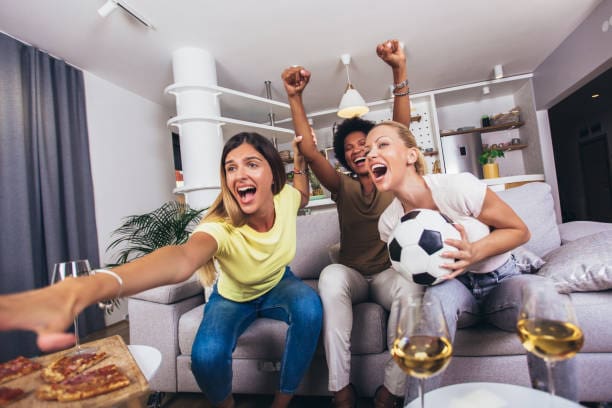 Group of female friends sitting at home cheering, watching a football game