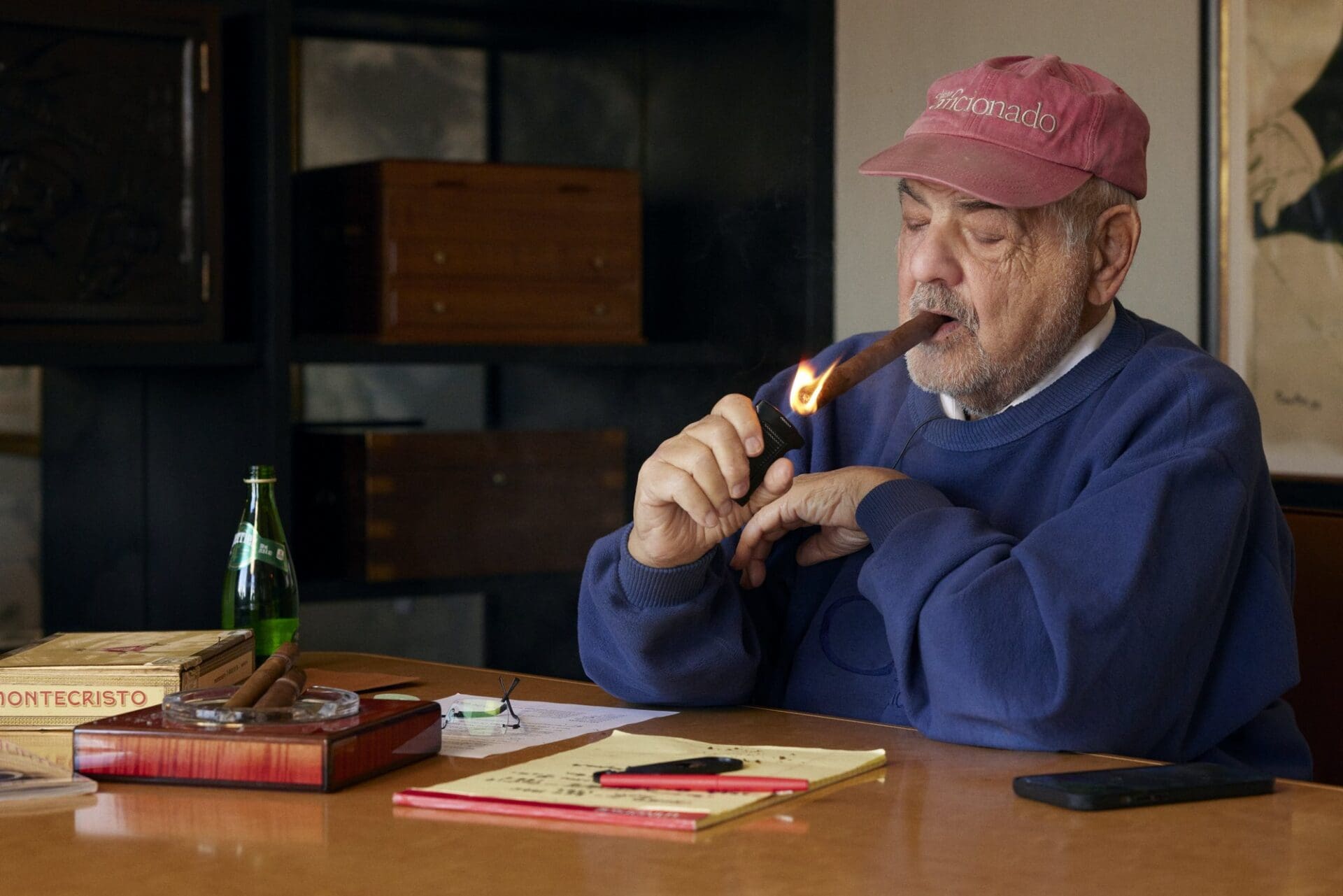 Marvin R. Shanken in a pink Cigar Aficionado cap lighting a cigar at a boardroom table